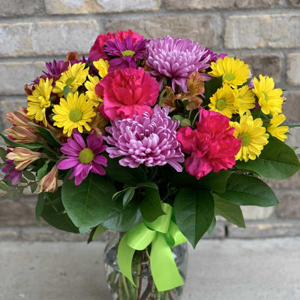 Colorful bouquet of daisies and carnations in a glass vase with a green ribbon
