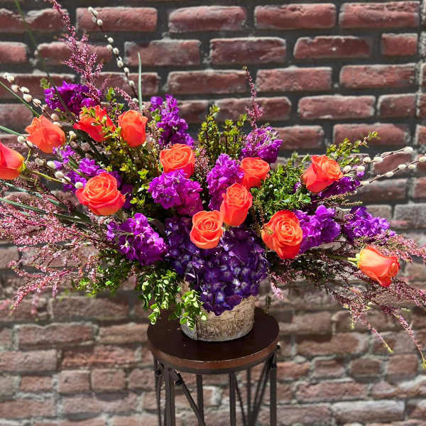 Orange roses and purple flowers in a rustic vase arrangement