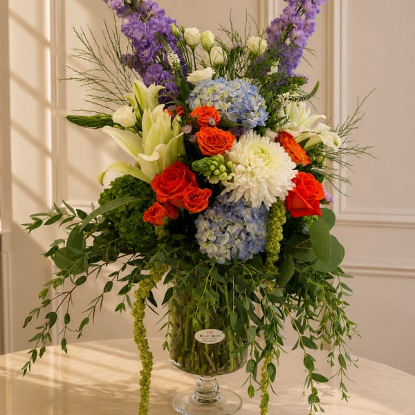 Tall mixed bouquet in a glass vase with purple, blue, white, and orange flowers