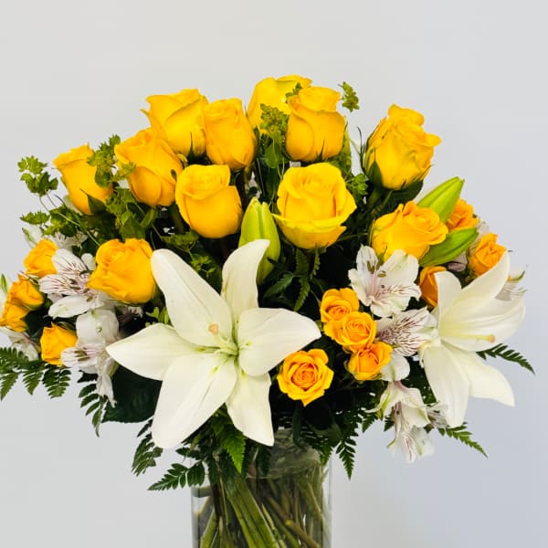 Yellow roses and white lilies arranged in a clear glass vase