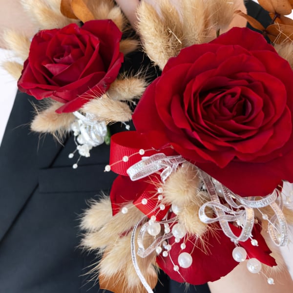 Red rose corsage with beige dried accents and ribbon on a wrist