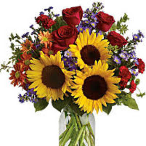 Bouquet of sunflowers, red roses, and mixed purple flowers in a glass vase