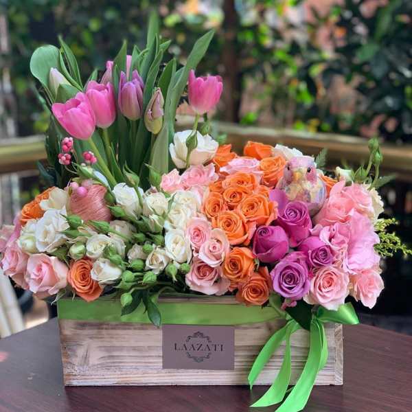 Mixed bouquet of pink tulips and roses in a wooden box with a green ribbon