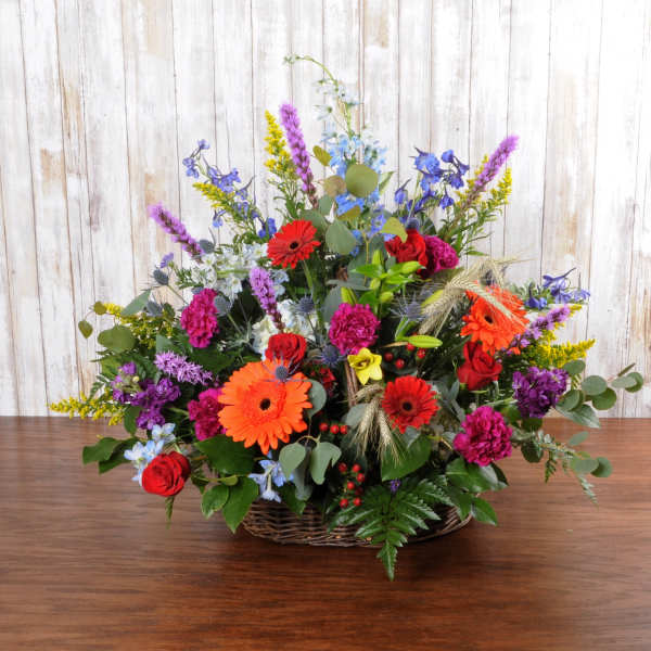 Colorful mixed flower arrangement with red roses and orange gerberas in a wicker basket.