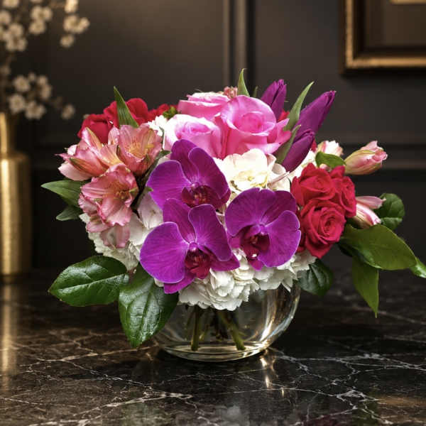 Mixed bouquet of pink roses, purple orchids, and white blooms in a glass bowl vase