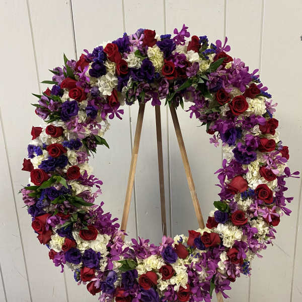 Large floral wreath of red, purple, and white blooms on a wooden easel