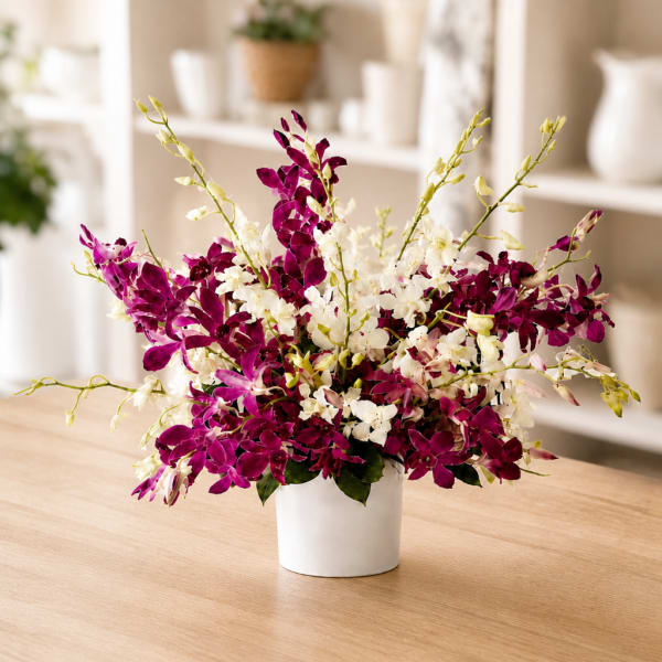 Purple and white orchid arrangement in a white pot on a table