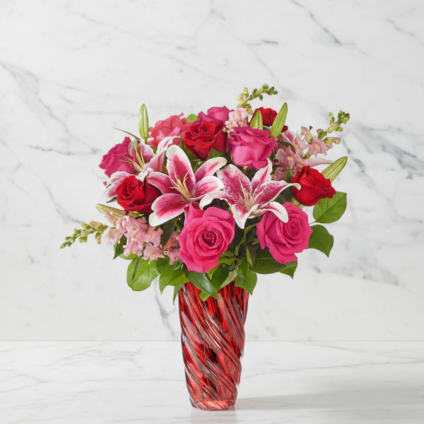 Pink and red roses with lilies in a red glass vase