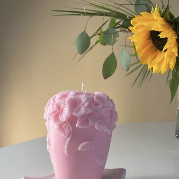 Pink floral candle on a white dish, with a sunflower arrangement in the background
