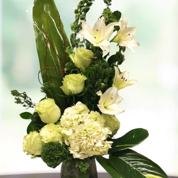White lilies and pale green flowers in a glass vase