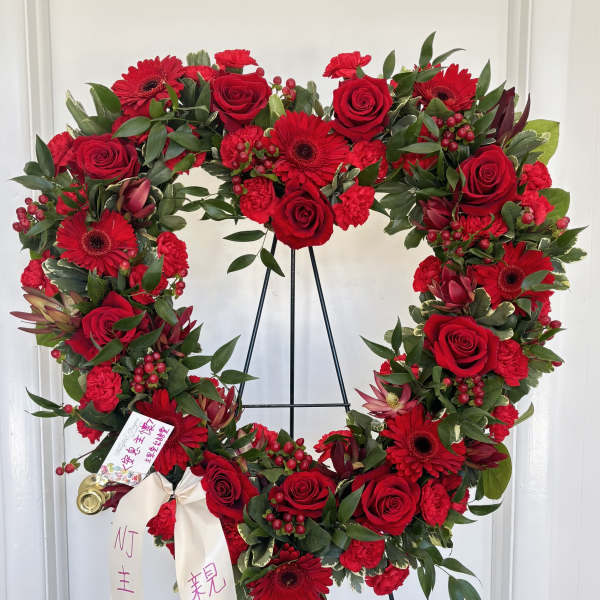 Large red floral heart wreath on a black stand with ribbon streamers.