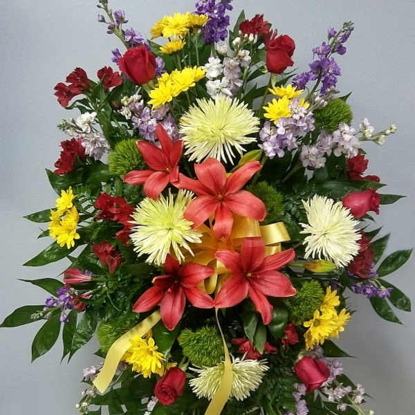 Standing floral spray with red lilies, yellow daisies, and purple accents