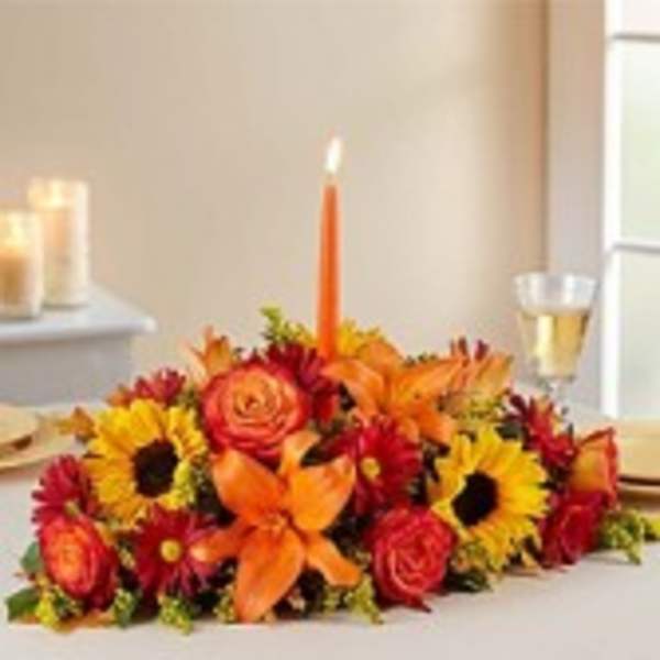Low floral centerpiece with orange lilies, sunflowers, and red roses around a candle