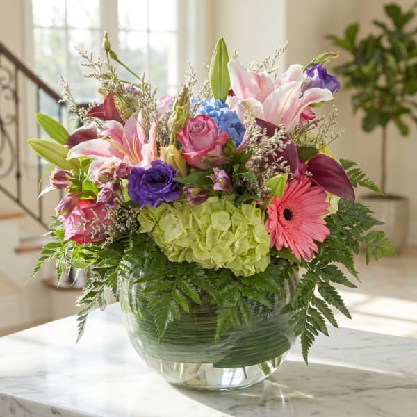 Mixed bouquet with lilies, roses, hydrangea, and a gerbera daisy in a glass vase