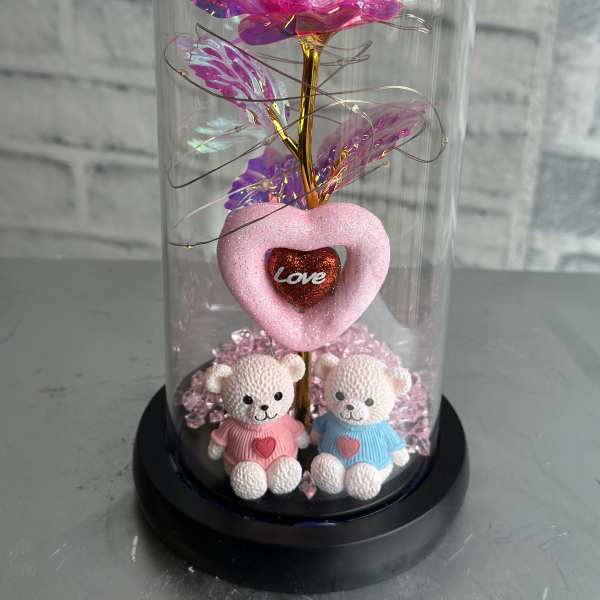 Pink iridescent artificial rose under a glass dome with two teddy bears