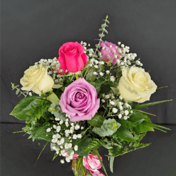 Small vase arrangement of cream, pink, and lavender roses with white filler flowers.