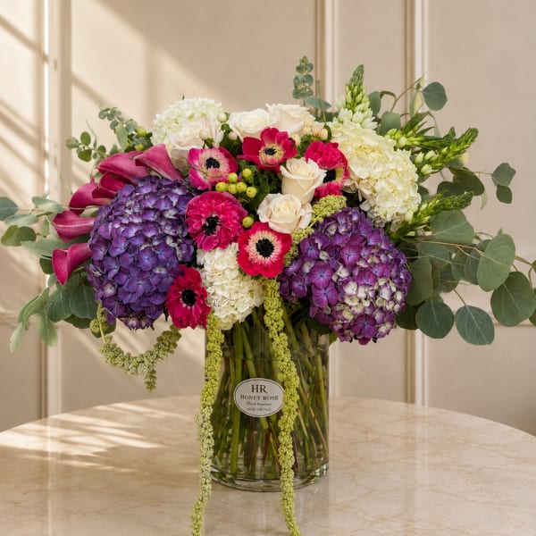 Bouquet of purple hydrangeas, pink anemones, and white roses in a glass vase