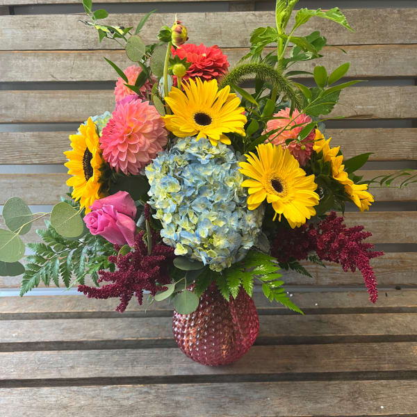 Mixed bouquet with sunflowers, pink dahlias, blue hydrangea, and a pink vase