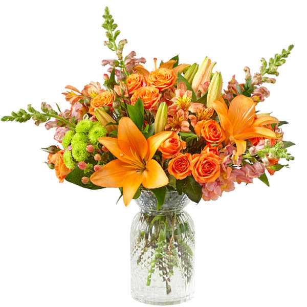 Orange lilies and roses arranged in a clear glass vase
