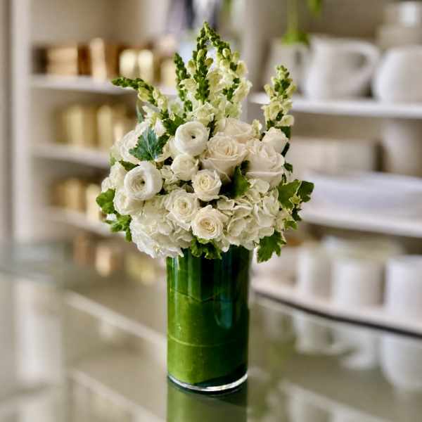 White roses and ranunculus in a tall green glass vase