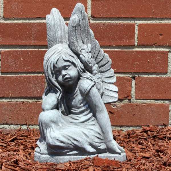 Gray angel statue of a seated child against a brick wall