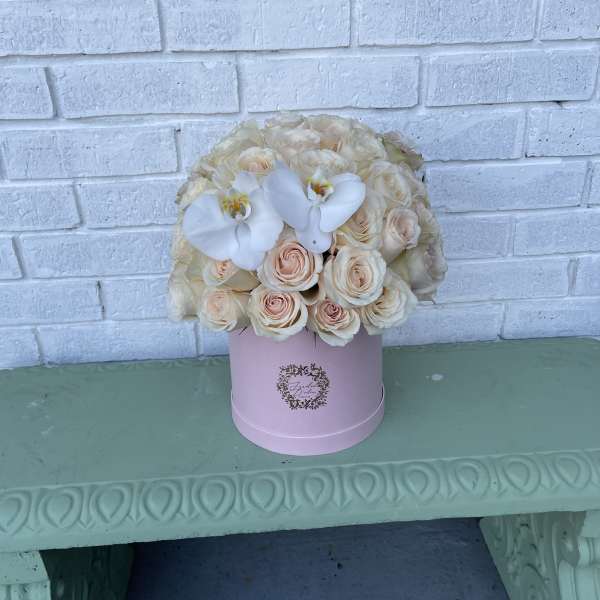 Cream roses and white orchids in a pink hat box