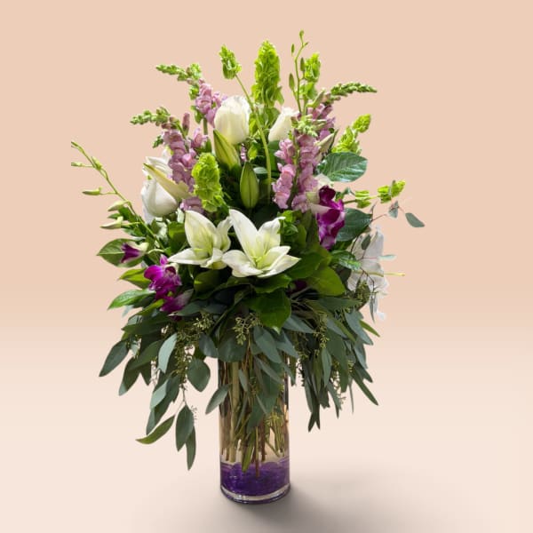 Tall bouquet of white lilies and purple flowers in a glass vase