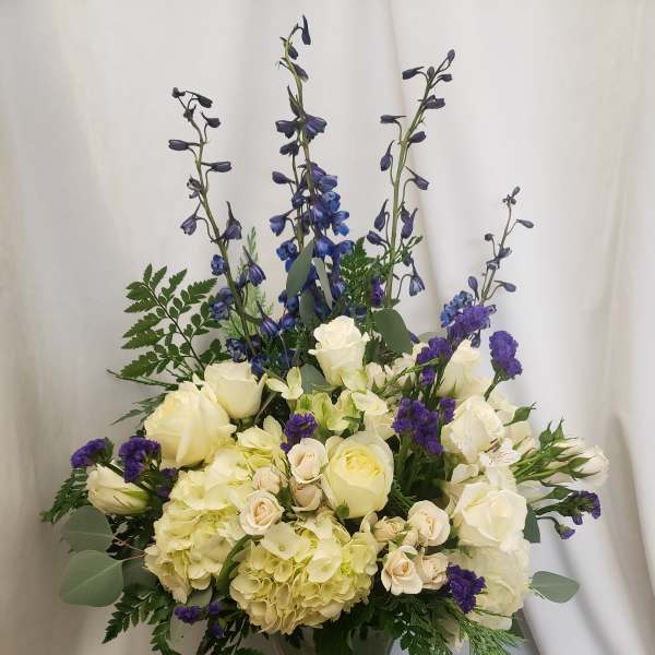 Tall bouquet of white roses, hydrangeas, and blue delphinium in a glass vase