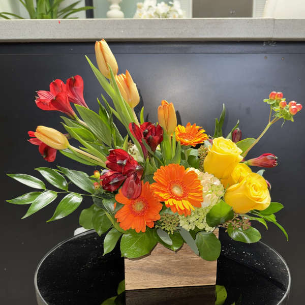 Mixed bouquet with yellow roses, gerbera daisies, and red-orange tulips in a wooden box