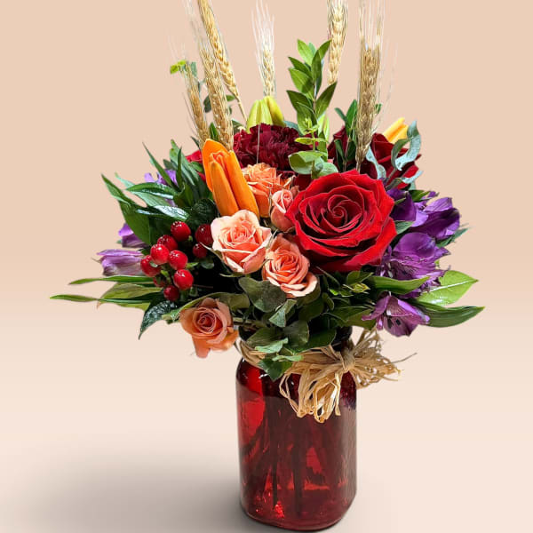 Mixed bouquet of red, peach, and purple flowers in a red glass vase