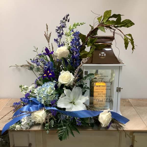 White roses and blue flowers arranged around a memorial lantern