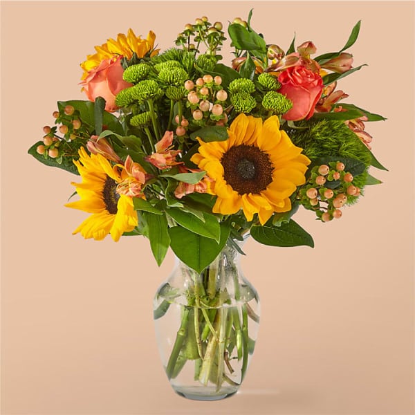 Bouquet of sunflowers, roses, and green button mums in a clear glass vase