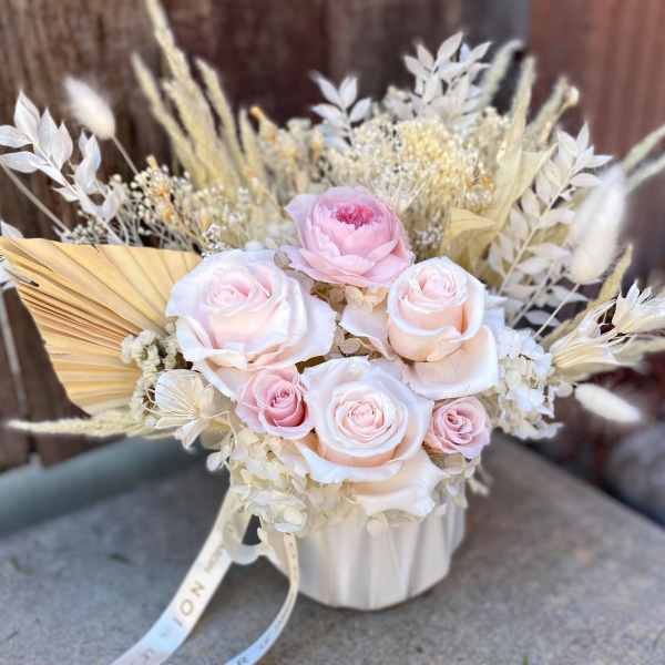 Pink and white roses arranged in a white vase with dried grasses