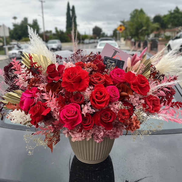 Large red and pink rose arrangement in a beige vase