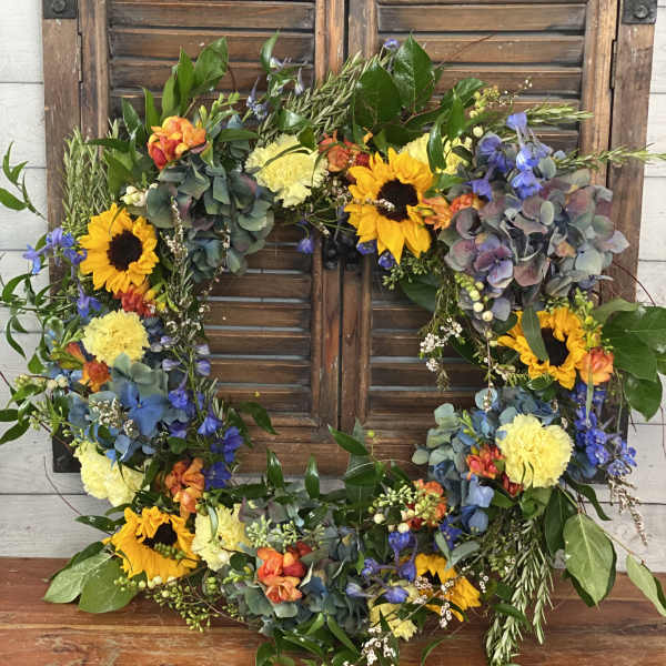 Floral wreath with sunflowers, blue blooms, and yellow carnations on a wooden shutter