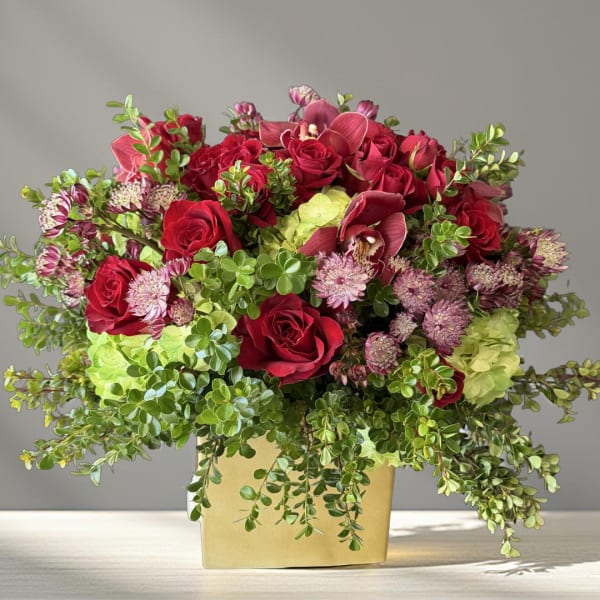 Red roses and pink flowers arranged in a gold box vase
