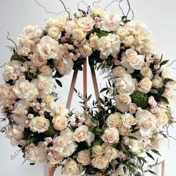 Large cream floral wreath on a wooden stand with trailing greenery