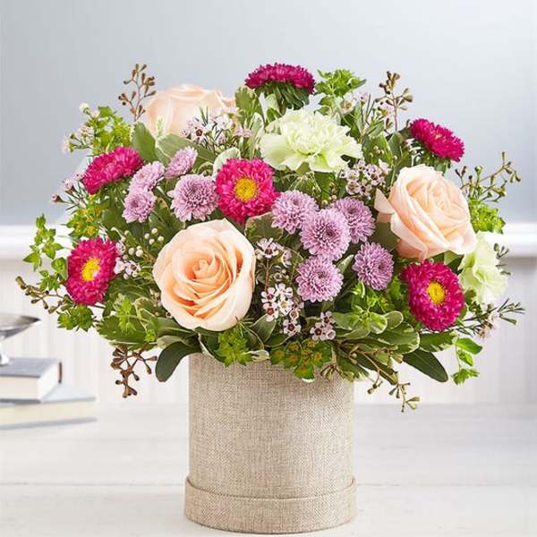 Peach roses and pink daisy-like flowers in a burlap-wrapped container