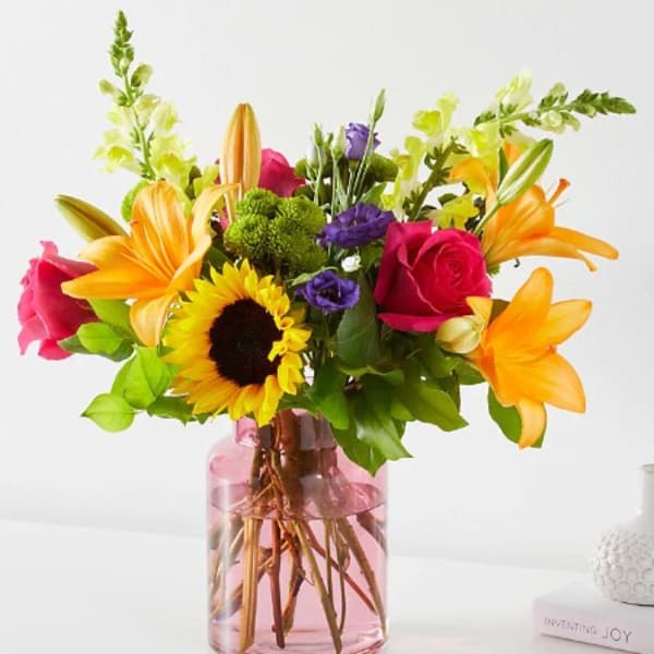 Mixed bouquet with roses, lilies, and a sunflower in a pink glass vase