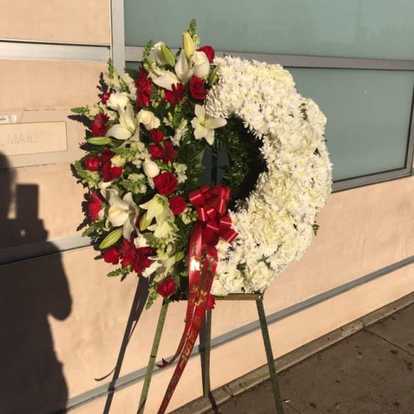 Large funeral wreath of white and red flowers on an easel with a red ribbon