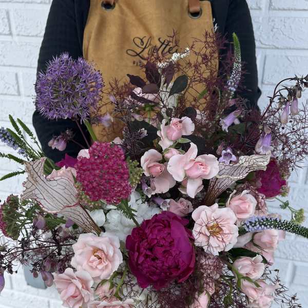 Large bouquet of pink and purple flowers held by a person in an apron