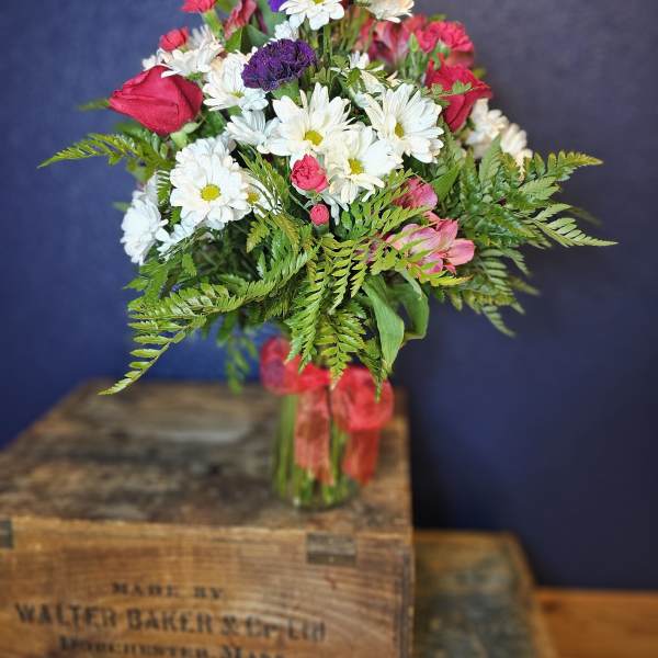 Bouquet of white daisies, pink roses, and purple blooms in a glass vase