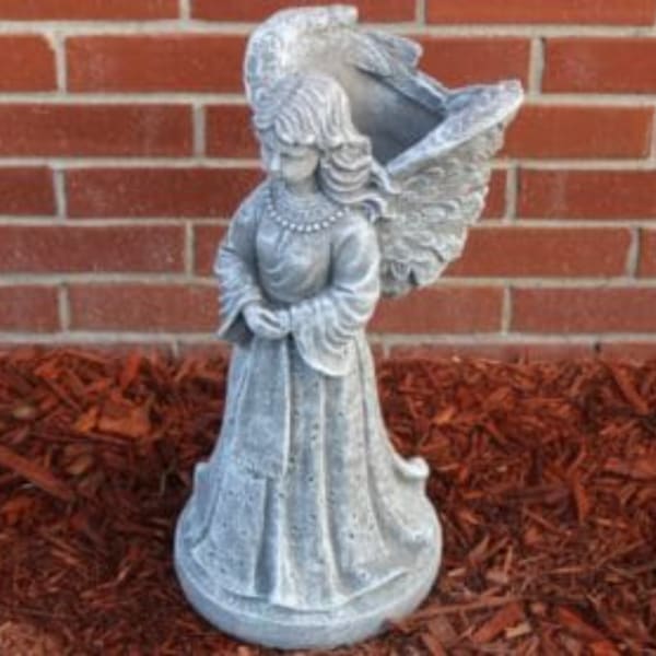 Silver angel statue standing against a brick wall
