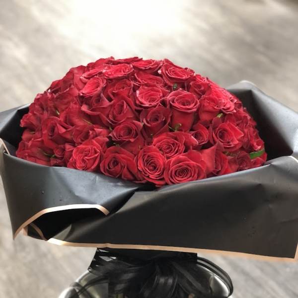 Large bouquet of red roses wrapped in black paper with a satin ribbon