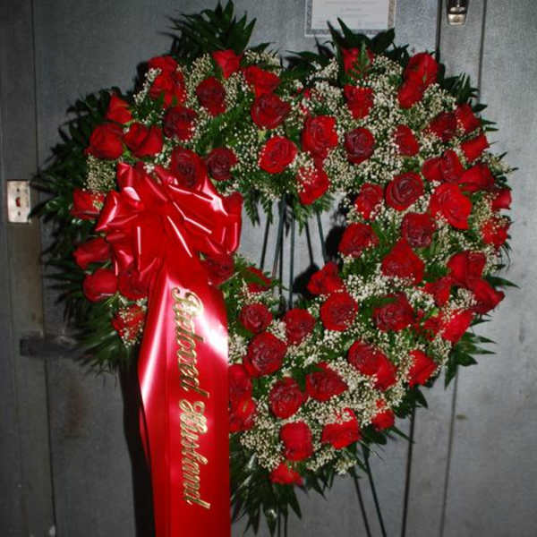 Heart-shaped red rose wreath on a stand with a red ribbon