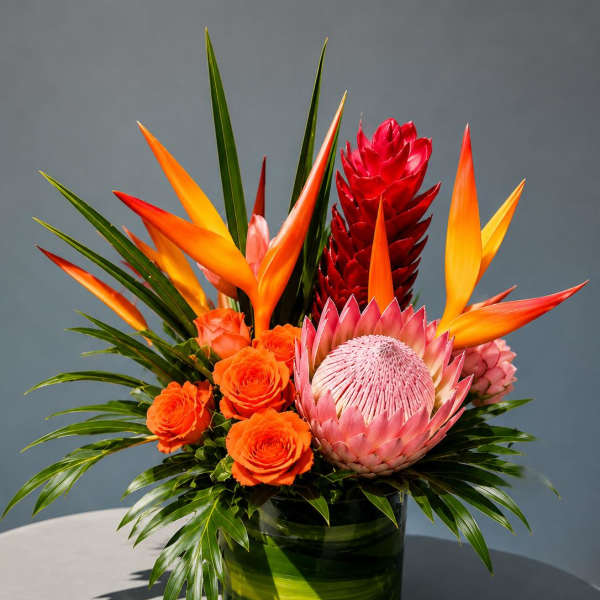 Tropical arrangement with orange roses and a pink protea in a green vase