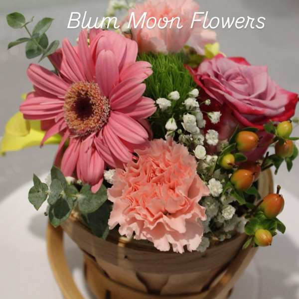Pink flowers arranged in a basket with a rose and gerbera daisy