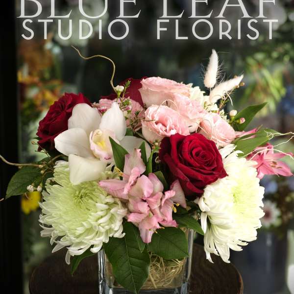 Bouquet of red and pink roses with white orchids in a glass vase