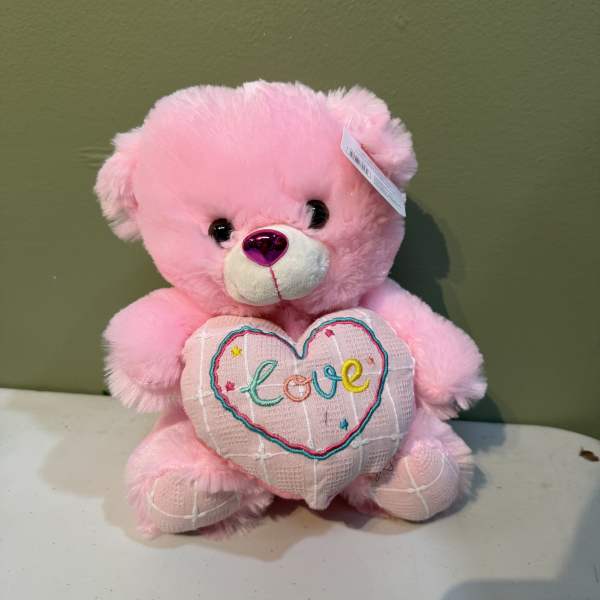 Pink teddy bear holding a heart with the word love