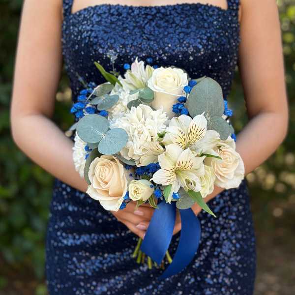Handheld bouquet of white flowers with blue accents and a ribbon